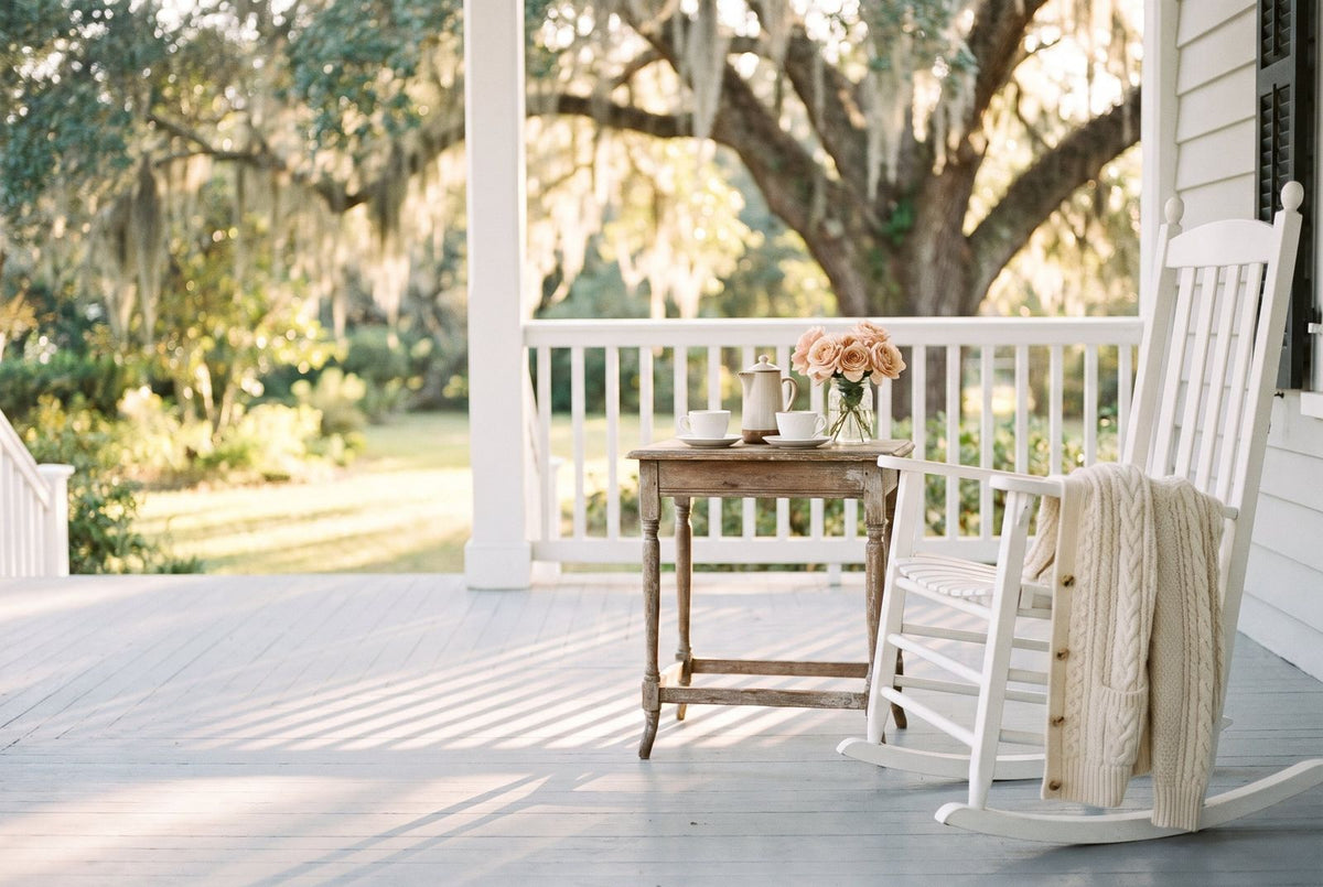 Two coffee cups on a porch table, a cable-knit cardigan over a rocking chair