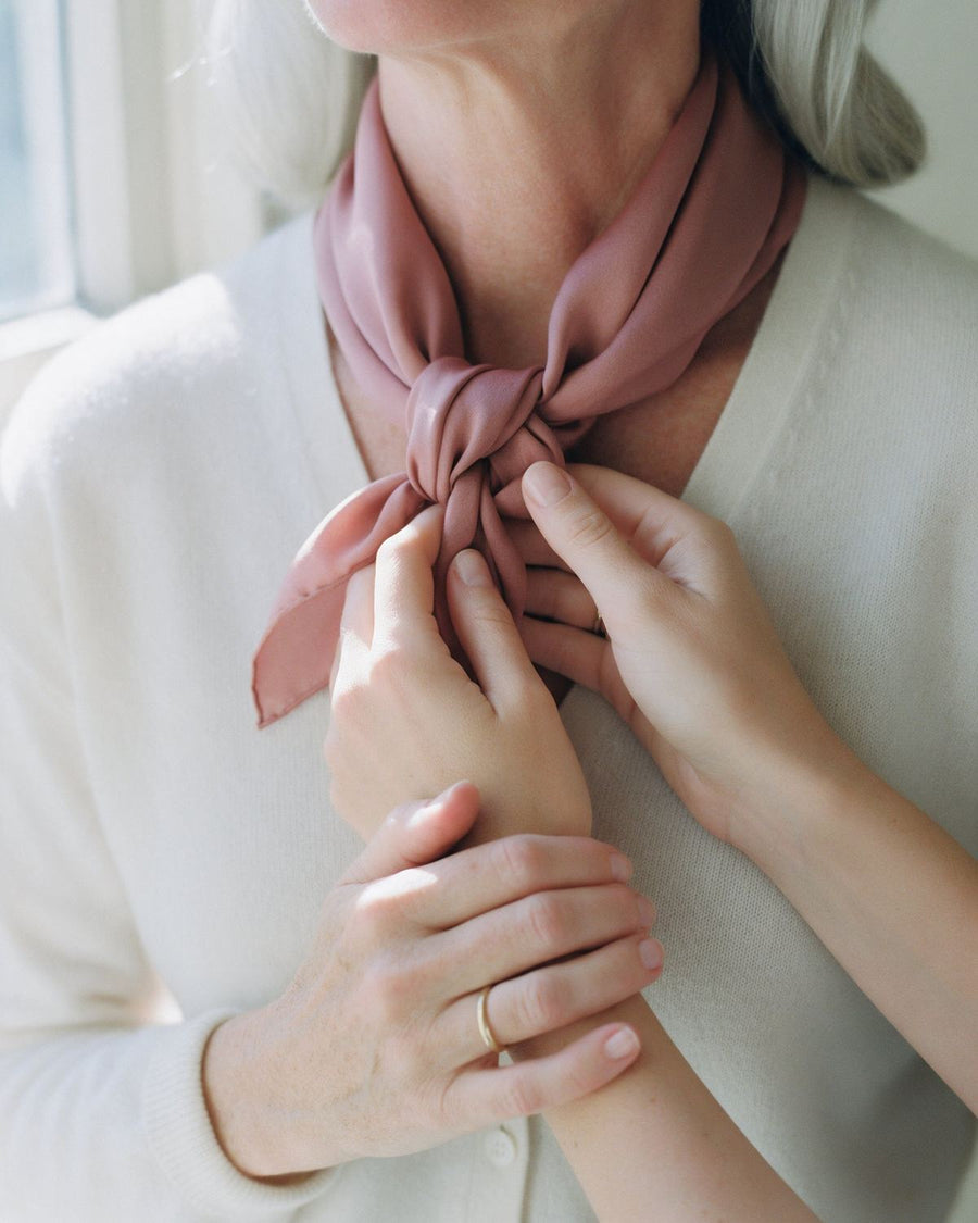 A daughter’s hands tying a rose silk scarf at her mother’s neck